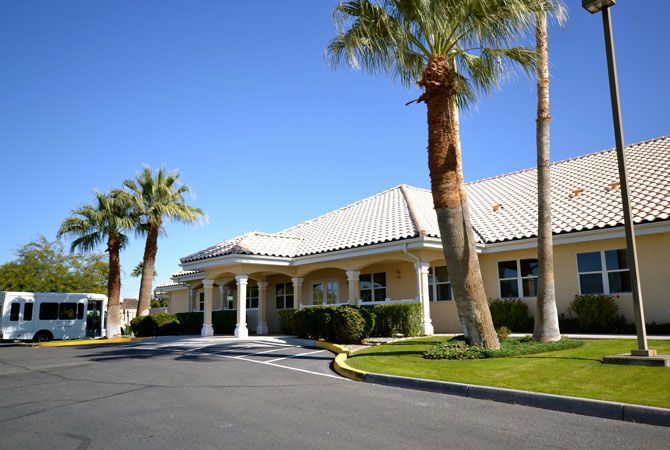 A sunny day view of a building entrance with palm trees and a clear blue sky.