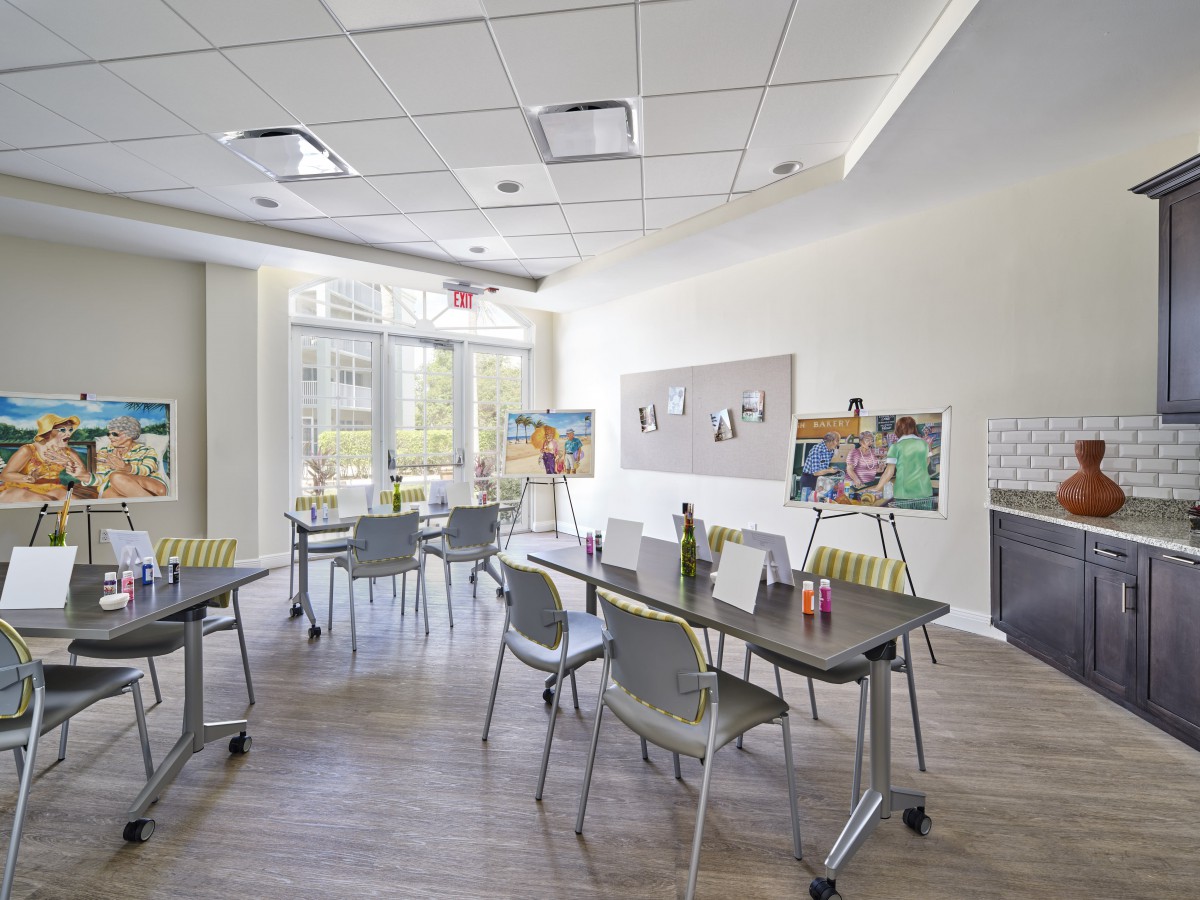 A modern classroom setup with tables and chairs arranged in a bright, open space featuring large windows and a whiteboard.