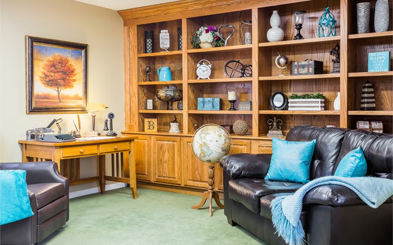 A cozy home office with a wooden bookshelf, desk, and comfortable armchair.