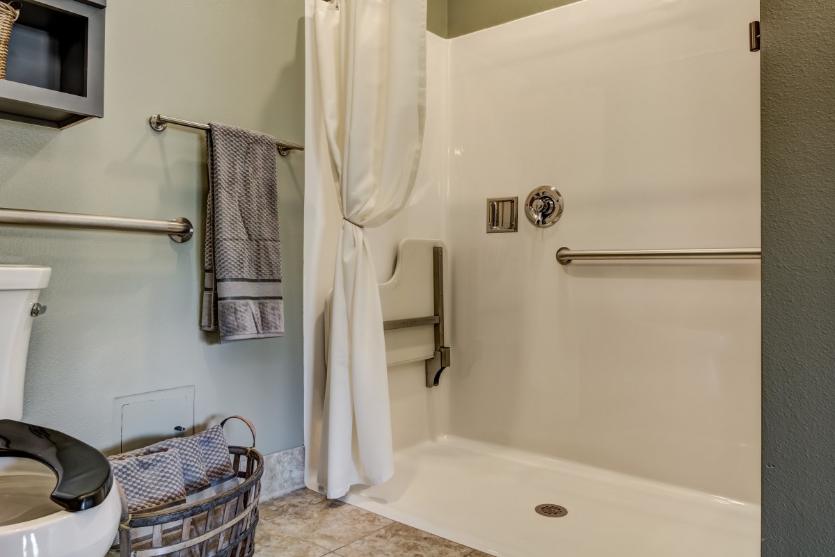 A modern bathroom with a shower area, grab bars, and neatly hung towels.
