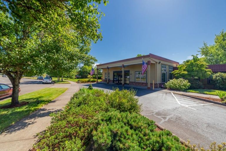 A small commercial building with a flag and landscaped greenery on a bright sunny day.