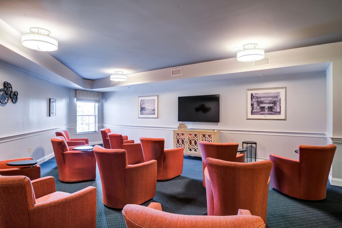 A modern meeting room with orange chairs arranged in a semi-circle facing a television, complemented by framed pictures on the walls and stylish lighting fixtures.