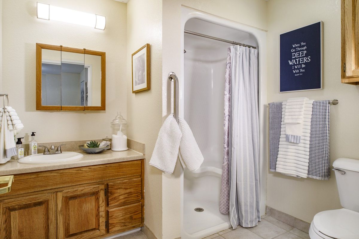 A clean and organized bathroom with a shower, sink, and wooden cabinet.