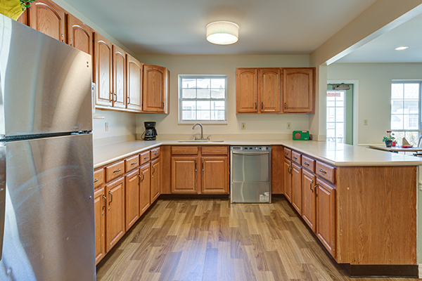 A spacious kitchen with wooden cabinets and a wooden floor, featuring modern appliances and ample natural light.