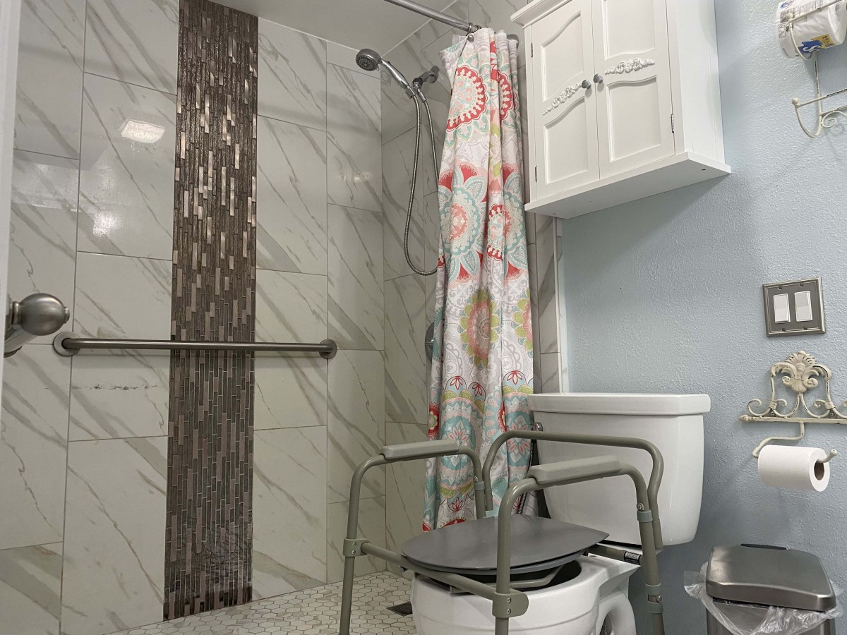 An accessible bathroom with a shower and grab bar, featuring a toilet with support rails.