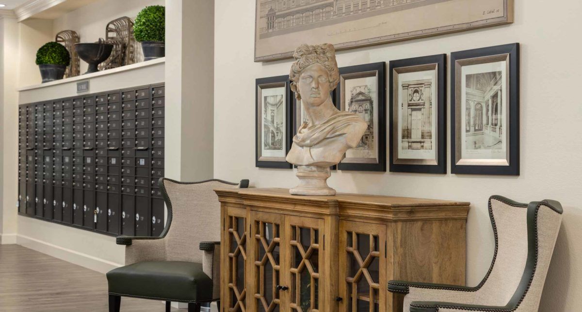 A classical bust sculpture placed on a wooden cabinet, surrounded by framed artwork in a stylish indoor setting.