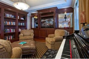 A cozy living room with a piano, surrounded by bookshelves and comfortable armchairs.