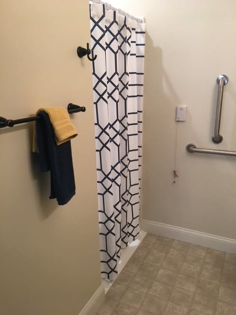 A bathroom featuring a patterned shower curtain, towel rack with towels, and a grab bar for accessibility.