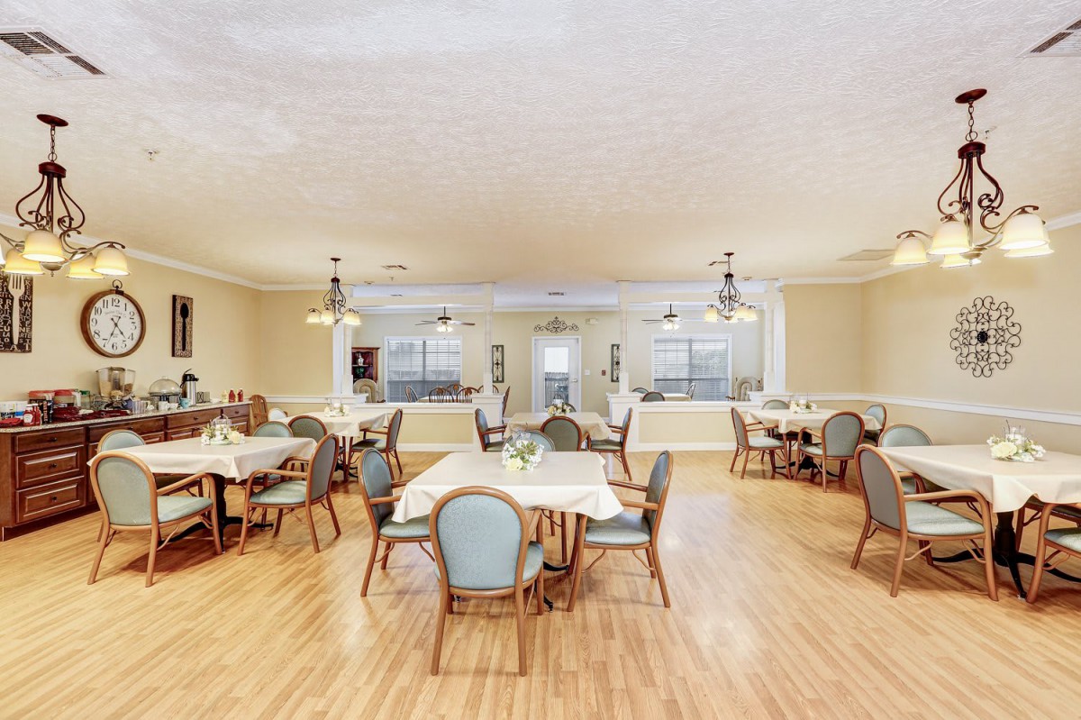 A spacious dining room with several tables and chairs, featuring warm lighting and wooden flooring.