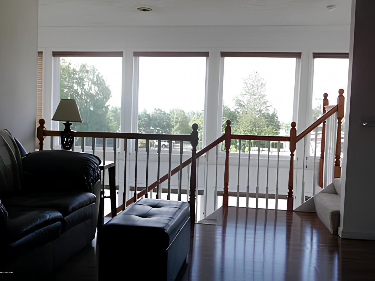 A bright living room with large windows and a view of trees, featuring a comfortable seating area and wooden stairs.