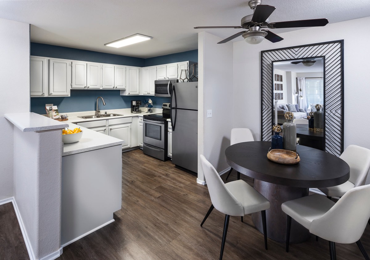 A modern kitchen and dining area with white cabinets, stainless steel appliances, and wood flooring.