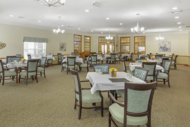 A spacious dining room with neatly arranged tables and chairs, featuring elegant lighting fixtures.