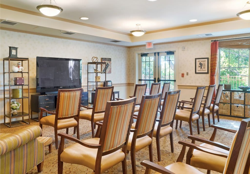 A well-arranged conference room featuring multiple chairs, a large television, and natural lighting.