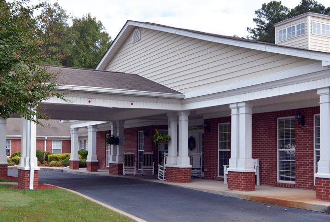 The image shows the entrance of a building with a covered porch supported by columns and a driveway leading up to it.