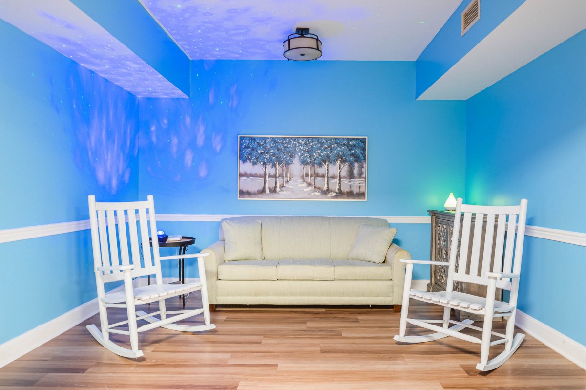 A cozy living room with blue walls, featuring a sofa and two white rocking chairs on a wooden floor.