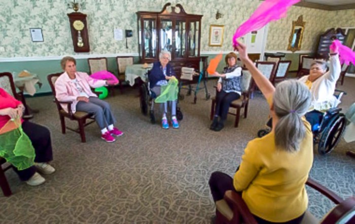 A group of seniors participating in an indoor exercise session with colorful scarves.