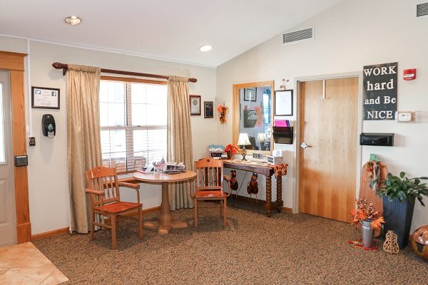 A cozy living room with a small dining table and chairs by the window, adorned with simple decor and warm lighting.