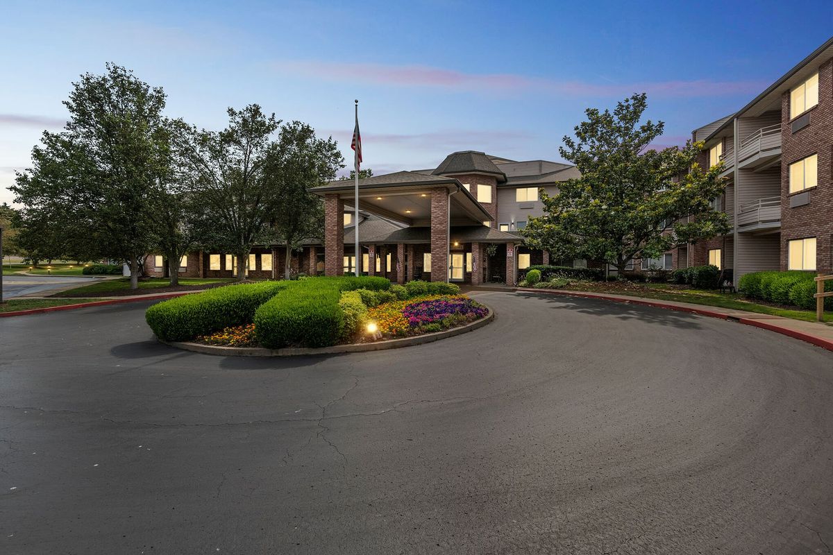 A scenic evening view of a building with a circular driveway and surrounding trees.