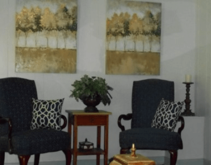A cozy seating area with two chairs, decorative pillows, a small table, a plant, and wall art.
