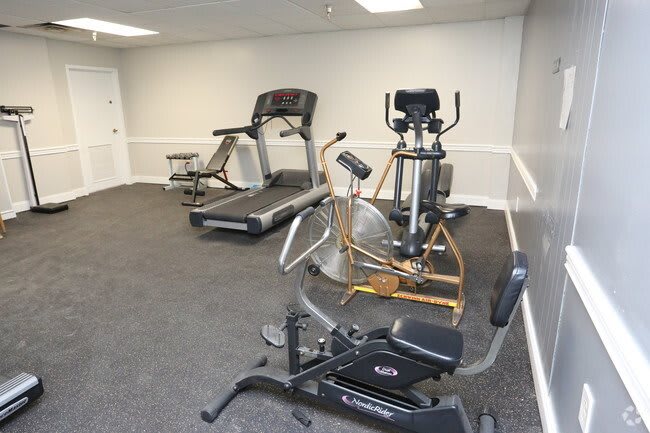 A compact gym with various exercise machines including a treadmill, elliptical, and cycling bike.