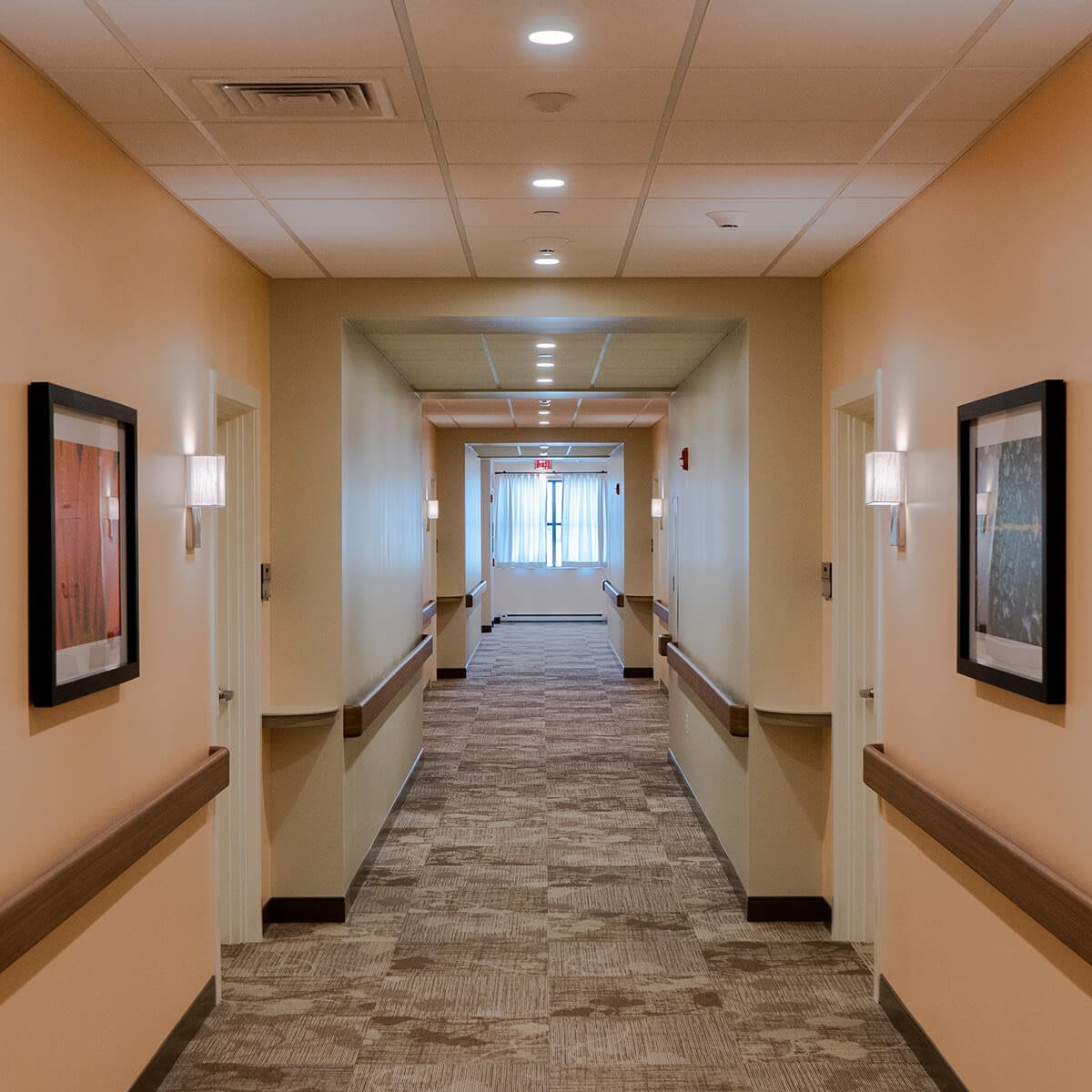 A well-lit corridor with carpeted flooring and artwork on the walls.