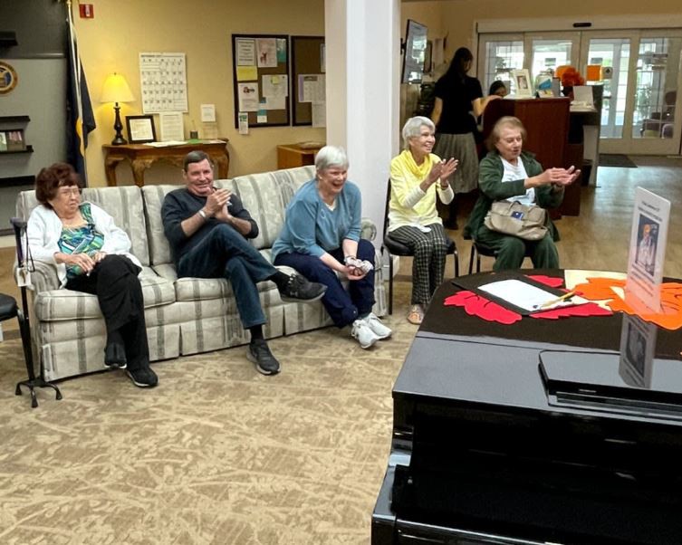 A group of people seated indoors, clapping at a social gathering.