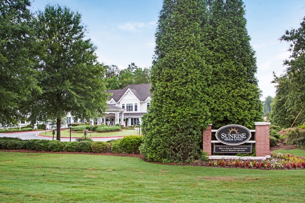 A large house with a driveway and landscaped garden, featuring a sign at the entrance.