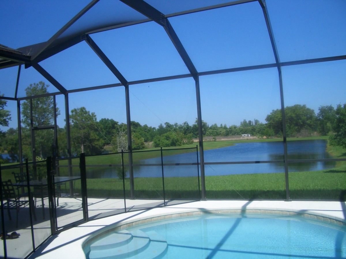 A screened-in swimming pool overlooking a scenic lake on a sunny day.