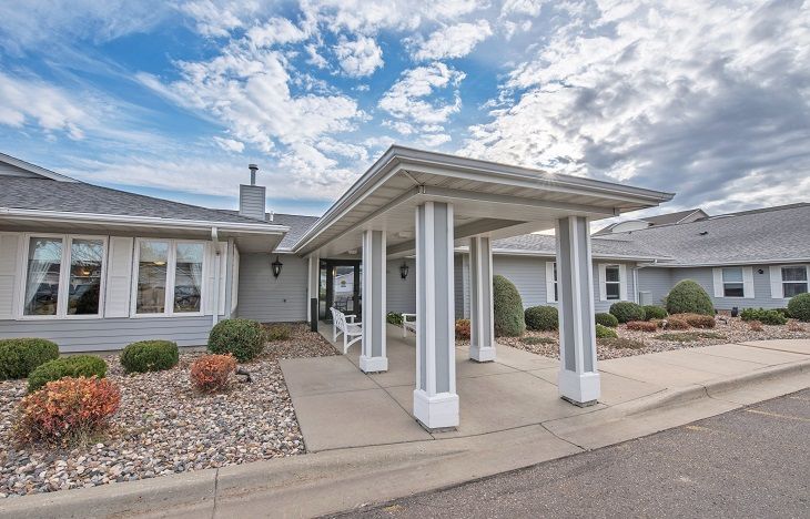 A residential building with a covered entrance and landscaped driveway under a partly cloudy sky.