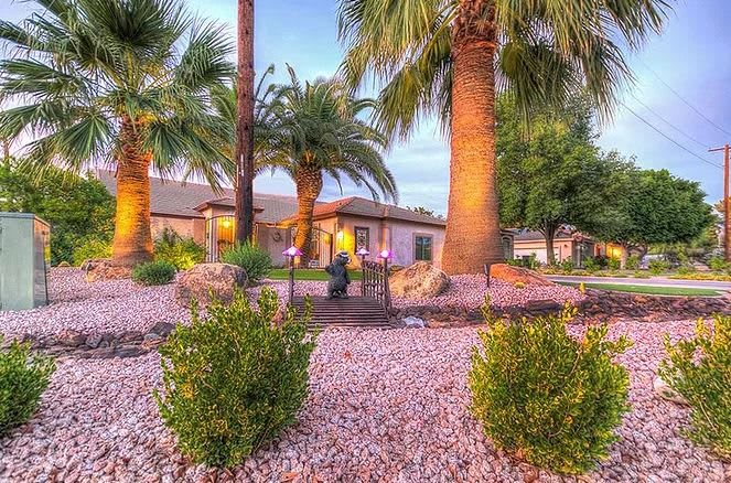 A beautiful house surrounded by palm trees and a well-maintained desert landscape at sunset.