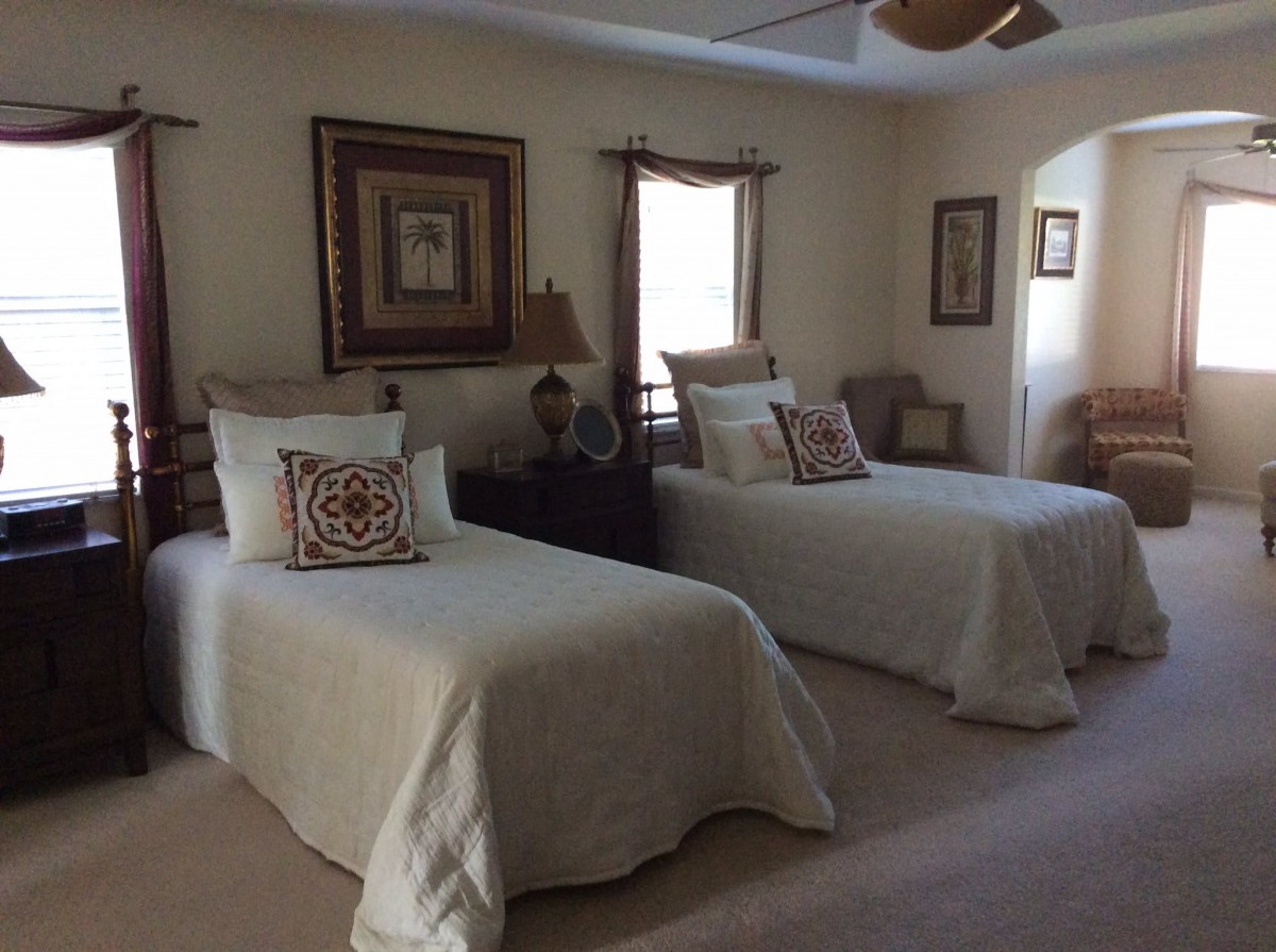 A cozy bedroom with two twin beds adorned with cushions, warm lighting, and stylish decor.