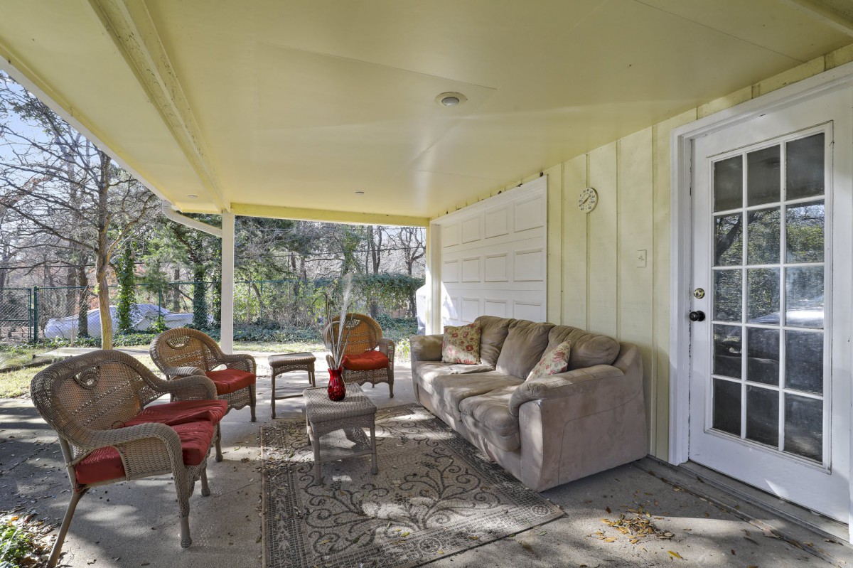 A cozy outdoor patio with comfortable seating, featuring a sofa, chairs, and a table under a covered porch.