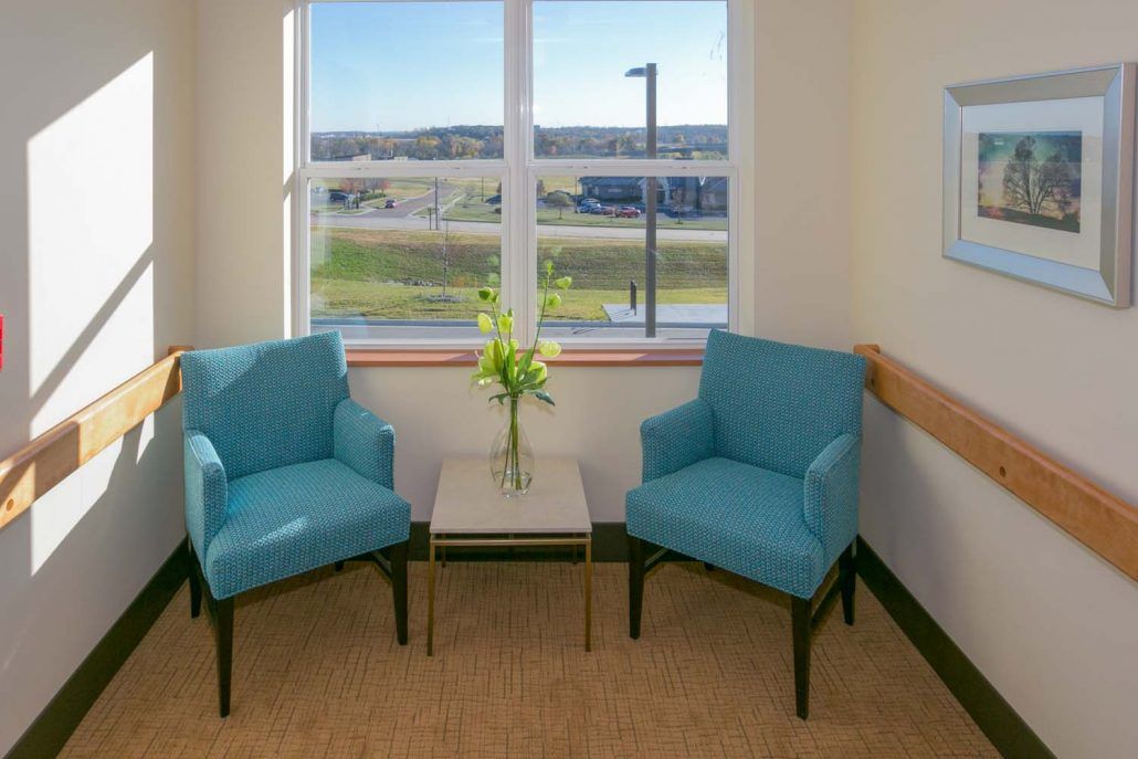 A cozy seating area with two blue chairs and a small table in front of a bright window.