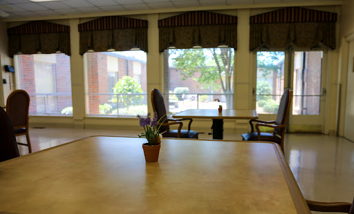 A serene interior space featuring a table and chairs, with natural light streaming in through large windows.