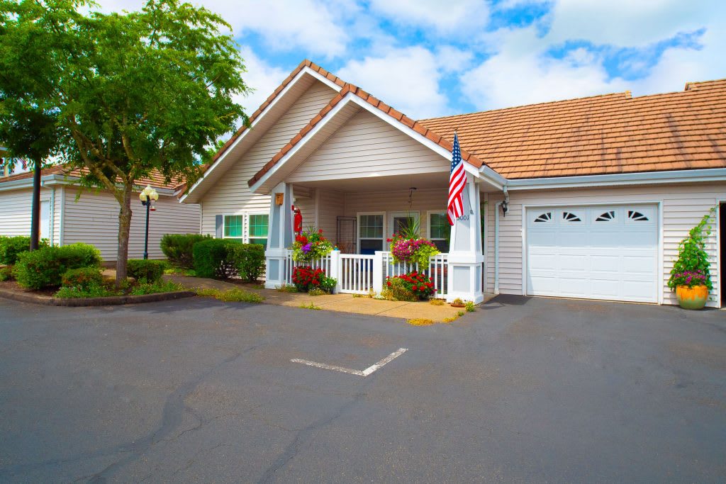 A charming suburban house with a garage and front porch, decorated with flags and surrounded by neat landscaping under a partly cloudy sky.