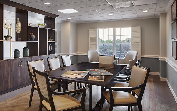 A modern meeting room with a conference table and chairs, featuring large windows and a bookshelf.