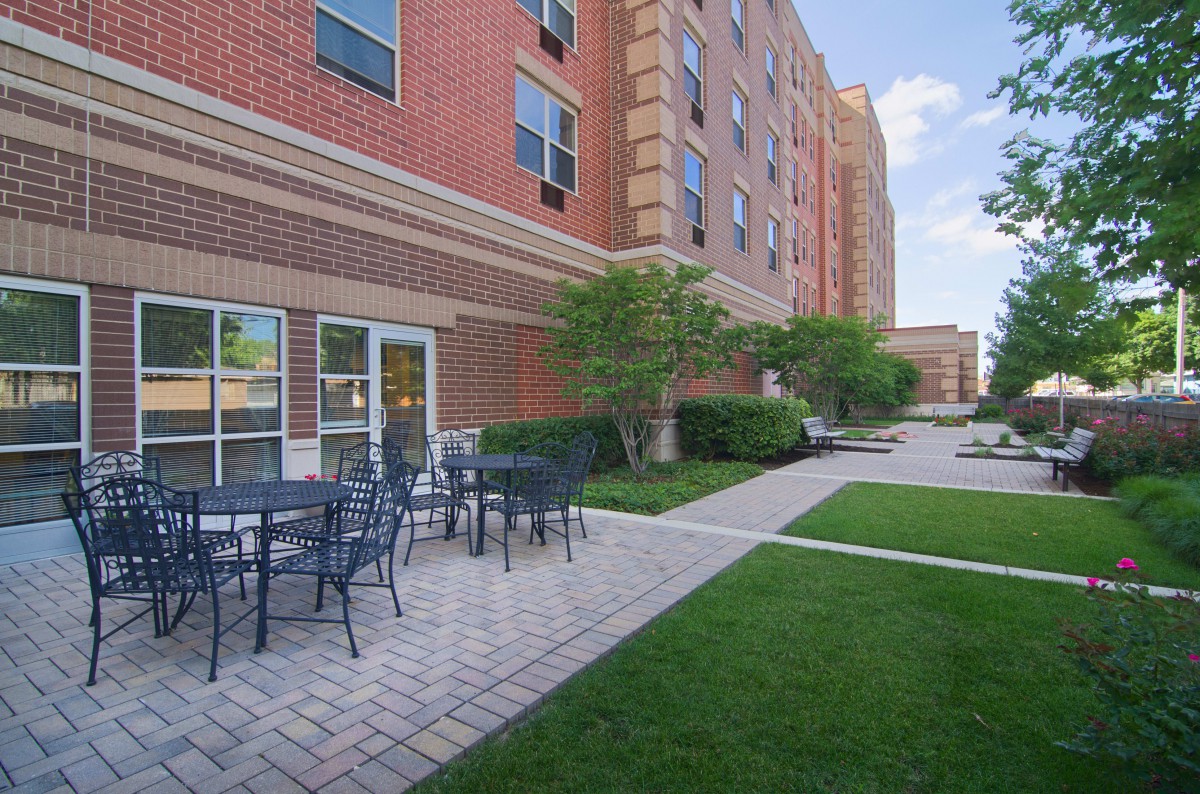 Outdoor patio area with tables and chairs next to a brick building.