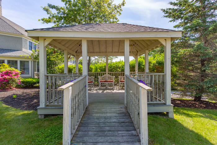 A wooden gazebo in a garden setting surrounded by greenery.