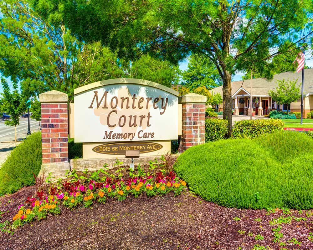 Entrance sign for Monterey Court Memory Care surrounded by lush landscaping.
