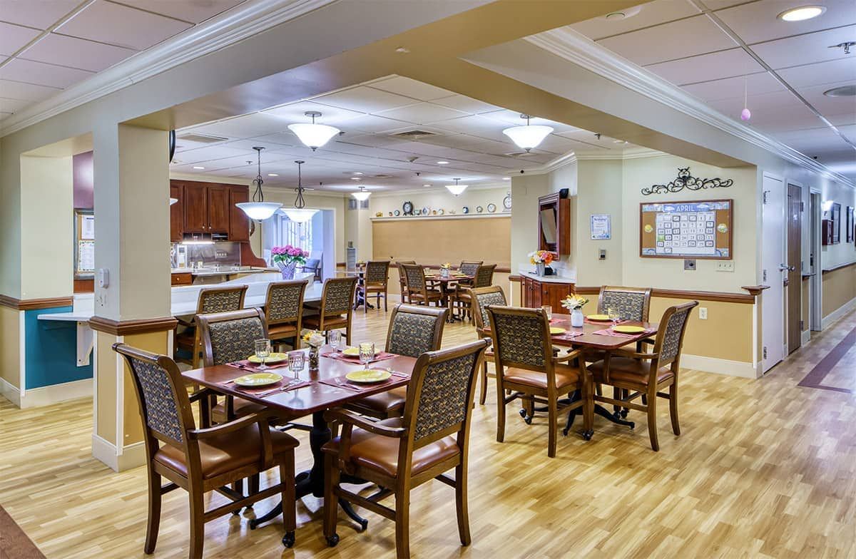 A well-lit dining area with neatly arranged tables and chairs, featuring warm wooden flooring.
