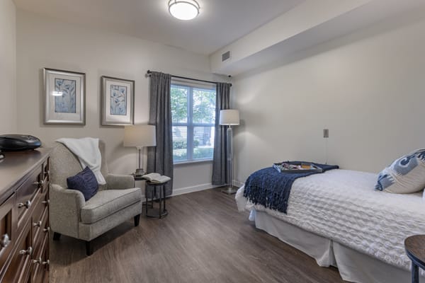 A cozy bedroom with modern decor, featuring a bed, armchair, and ample natural light.