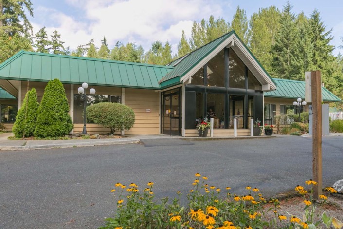 A modern building with a green roof surrounded by trees and flowers.
