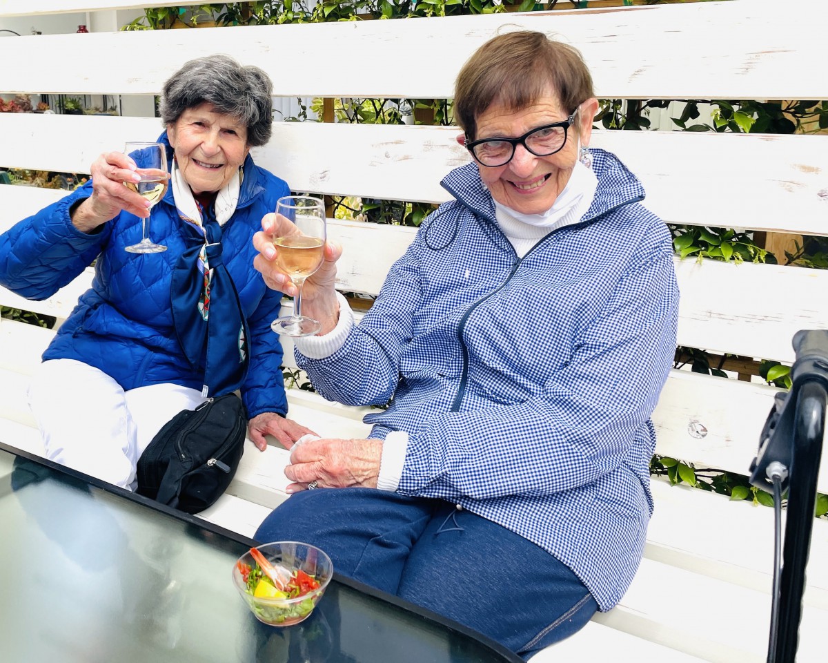 Two elderly women enjoying a celebratory drink outdoors.