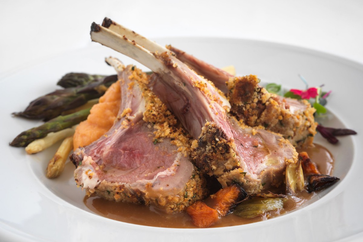 A gourmet rack of lamb served with a side of vegetables.