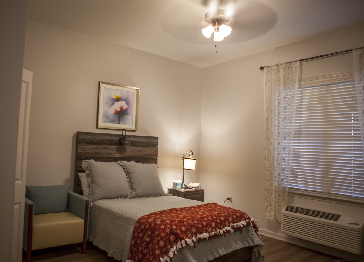 A cozy bedroom with a neatly made bed, a bedside lamp, and artwork on the wall.
