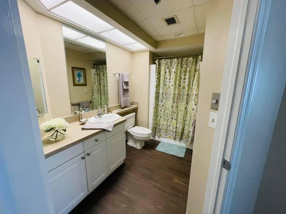 A clean and well-organized bathroom featuring a large mirror, sink with countertop, toilet, and shower with a floral curtain.