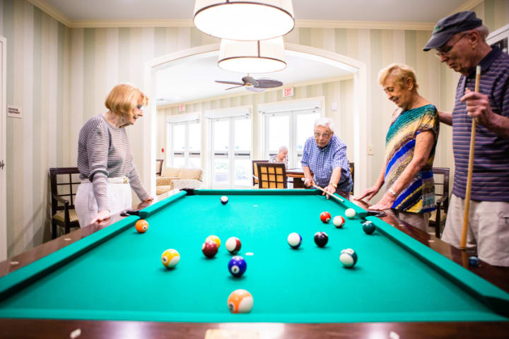 A group of elderly individuals enjoying a game of billiards in a bright, inviting room.