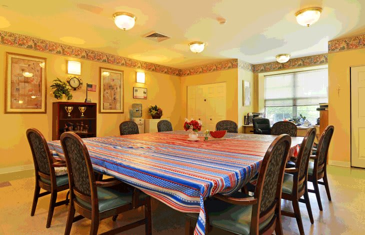 A well-lit dining room with a large table covered by a colorful striped tablecloth, surrounded by chairs.