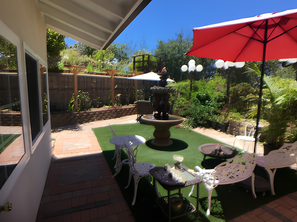A sunny backyard featuring a fountain, outdoor seating, and vibrant garden.
