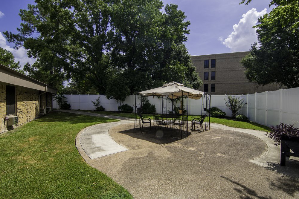 A sunny outdoor patio area with a table and umbrella surrounded by a garden and trees.